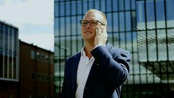 ung stilig caucasian affärsman stående i stad företag distrikt talande på cell telefon video