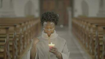 Young african woman praying inside church holding a candle light video