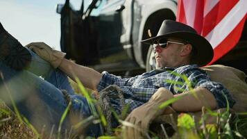patriottisch Amerikaans boer in cowboy hoed en vliegenier stijl zonnebril aan het liegen in de veld- ontspannende na werken dag Bij zijn landbouwgrond. video