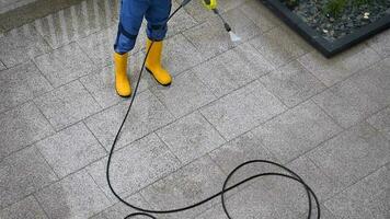 arbeider in geel rubber laarzen druk het wassen beton plaat oprit in voorkant van woon- huis gedurende regelmatig onderhoud activiteiten. video