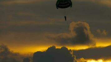 largo disparo, personas volador en un paracaídas en contra un ardiente nublado puesta de sol. extremo Deportes, parapente recreativo aventuras deporte video