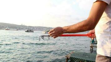 pescatore pesca su mare, uomo prendere pesca asta per pesca a tramonto mare e paesaggio urbano, selettivo messa a fuoco video