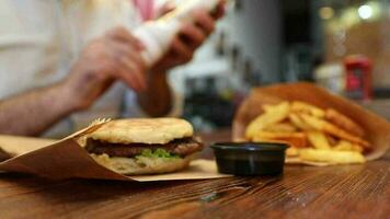 Man trying to squeeze mayonnaise on a hamburger and french fries standing on the table, the image of man-eating fast food in the restaurant video