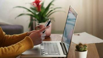 Young female using mobile phone and laptop technology, checking cellphone while remote working in office. video