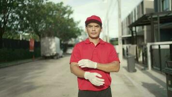 portret. een pakket levering arbeider gekleed in rood uniform is kruispunt zijn armen en op zoek Bij de camera. video