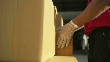 un paquete o empaquetar entrega trabajador vestido en un rojo uniforme es levantamiento un paquete desde el maletero de el camión a el recipiente. contacto el receptor en frente de el casa. video