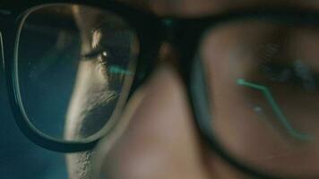 Woman in glasses looking on the monitor and and working with charts and analytics. The monitor screen is reflected in the glasses. Work at night. Extreme close-up video