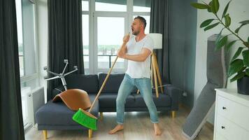 hombre limpieza el casa, teniendo divertido bailando y canto con un escoba. video