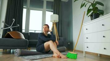 mujer se sienta en el medio de el habitación profundo en pensamiento. ella necesidades a limpiar arriba, pero ella procrastina video