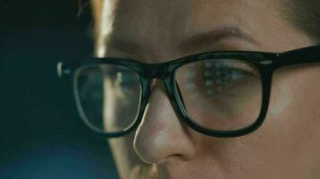 Woman in glasses looking on the monitor and and working with charts and analytics. The monitor screen is reflected in the glasses. Work at night. Extreme close-up video