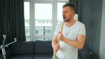 Man cleaning the house, having fun dancing and singing with a broom. video
