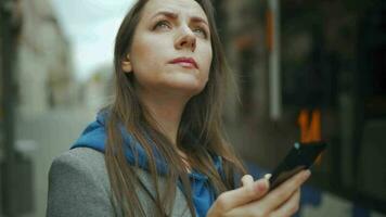 Woman stands at a public transport stop and checks the timetable. Tram pulls up in the background video