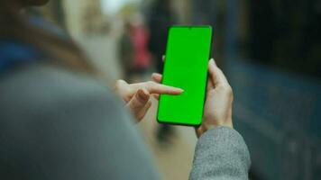 femme à le rue en utilisant téléphone intelligent avec vert maquette écran dans verticale mode contre le toile de fond de une qui passe tram video