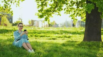 kvinna använder sig av smartphone medan Sammanträde i parkera efter efterbehandling utomhus- arbete på solnedgång video