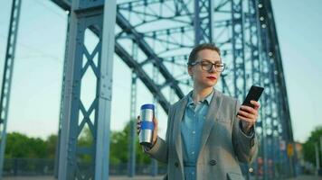 Caucasian businesswoman in a coat walking around the city in the early morning and using smartphone. Communication, work day, busy life concept video