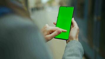 femme à le rue en utilisant téléphone intelligent avec vert maquette écran dans verticale mode contre le toile de fond de une qui passe tram video