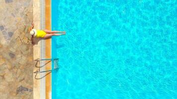 antenne visie van een vrouw in geel zwempak en een hoed zit Aan de rand van de zwembad video