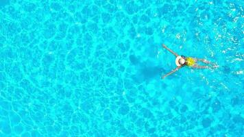 Aerial view of a woman in yellow swimsuit swimming in the pool. Summer lifestyle video