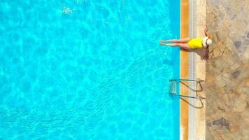 aéreo Visão do uma mulher dentro amarelo roupa de banho e uma chapéu senta em a Beira do a piscina video