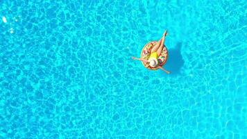 Aerial view of a woman in yellow swimsuit lying on a donut in the pool video