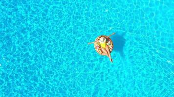 Aerial view of a woman in yellow swimsuit lying on a donut in the pool video