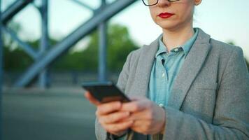 Caucasian businesswoman in a coat walking around the city in the early morning and using smartphone. Communication, work day, busy life concept video