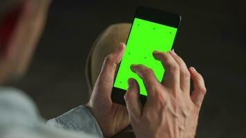 Man using smartphone with green mock-up screen in vertical mode and stroking the fluffy cat. Man browsing Internet video