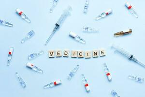 Flat lay medicine from wooden letters on a blue background. Ampoules and syringes. Vaccination photo