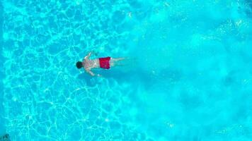 Aerial view of a man in red shorts swimming in the pool, slow motion video