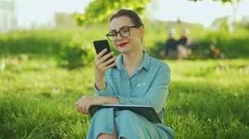 femme en utilisant téléphone intelligent tandis que séance dans parc après finition Extérieur travail à le coucher du soleil video