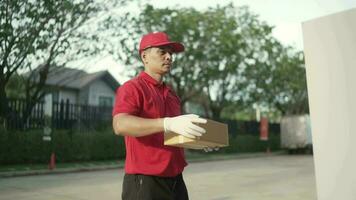 een pakket levering arbeider gekleed in een rood uniform is Holding een pakket doos en rinkelen de klok voor de ontvanger. contact de ontvanger in voorkant van de huis. video