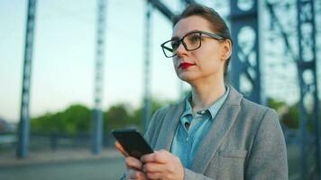 mujer en un abrigo, caminando alrededor el ciudad en el temprano Mañana y utilizando teléfono inteligente, lento movimiento video