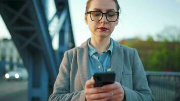 vrouw in een jas, wandelen in de omgeving van de stad in de vroeg ochtend- en gebruik makend van smartphone, langzaam beweging video