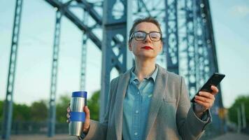 Frau im ein Mantel, Gehen um das Stadt im das früh Morgen, Trinken Kaffee und mit Smartphone, schleppend Bewegung video