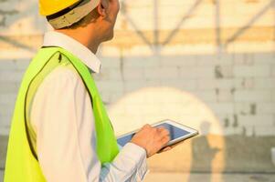 An Asian engineer man is wearing a protective helmet on head, using tablet Analytics engineering data photo