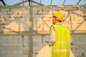 An Asian engineer man is wearing a protective helmet on head, using tablet Analytics engineering data photo
