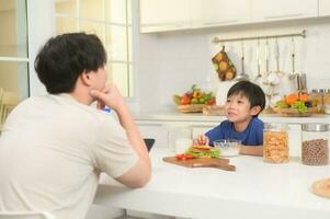 contento joven asiático padre y hijo comiendo sano comida en cocina a hogar foto