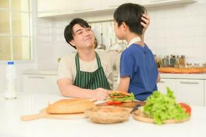 Happy Young Asian father giving support to his son  in kitchen at home photo