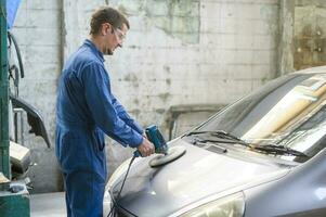 caucásico hombre es utilizando coche pulido máquina en reparar mecánico pintura tienda foto