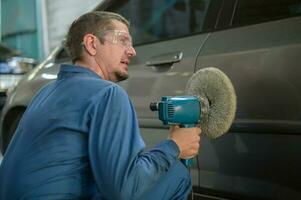 caucásico hombre es utilizando coche pulido máquina en reparar mecánico pintura tienda foto