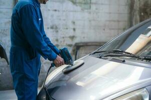 de cerca hombre mano es utilizando coche pulido máquina en reparar mecánico pintura tienda foto