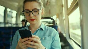 kvinna i spårvagn använder sig av smartphone chattar och textning med vänner. stad, urban, transport. långsam rörelse video