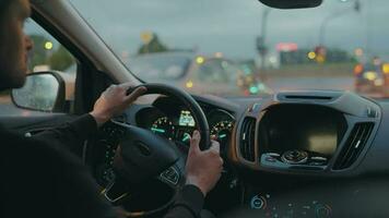 Man driving car through the streets of evening city. City lights, cars, traffic lights, buildings in the window of the car. video