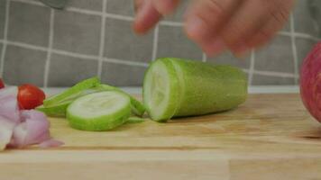 Female hand using a knife to slice cucumbers on a cutting board. Close-up. Woman with kitchen knife cutting cucumber at home. Preparing homemade food video