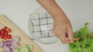 cucinando - donna fabbricazione fresco biologico verdura insalata nel il cucina. femmina mani preparazione delizioso salutare cibo a casa, miscelazione verdure nel un' ciotola, avvicinamento. video