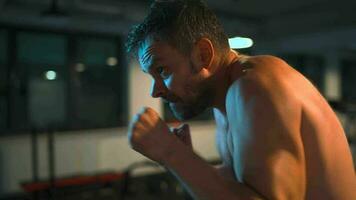 Alone boxer is working out blows on a punching bag in a gym in evening video