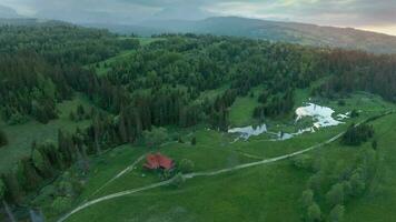 aereo Visualizza di un' estate montagna paesaggio con un' Casa e un' fiume nel il primo piano e rocce coperto di nuvole nel il sfondo video