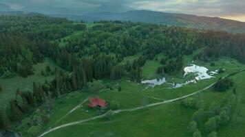 Antenne Aussicht von ein Sommer- Berg Landschaft mit ein Haus und ein Fluss im das Vordergrund und Felsen bedeckt durch Wolken im das Hintergrund video