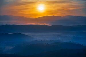 Mountain range with visible silhouettes through the morning colorful fog photo