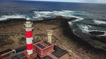 faro en un rocoso costa, volador alrededor en un círculo. video